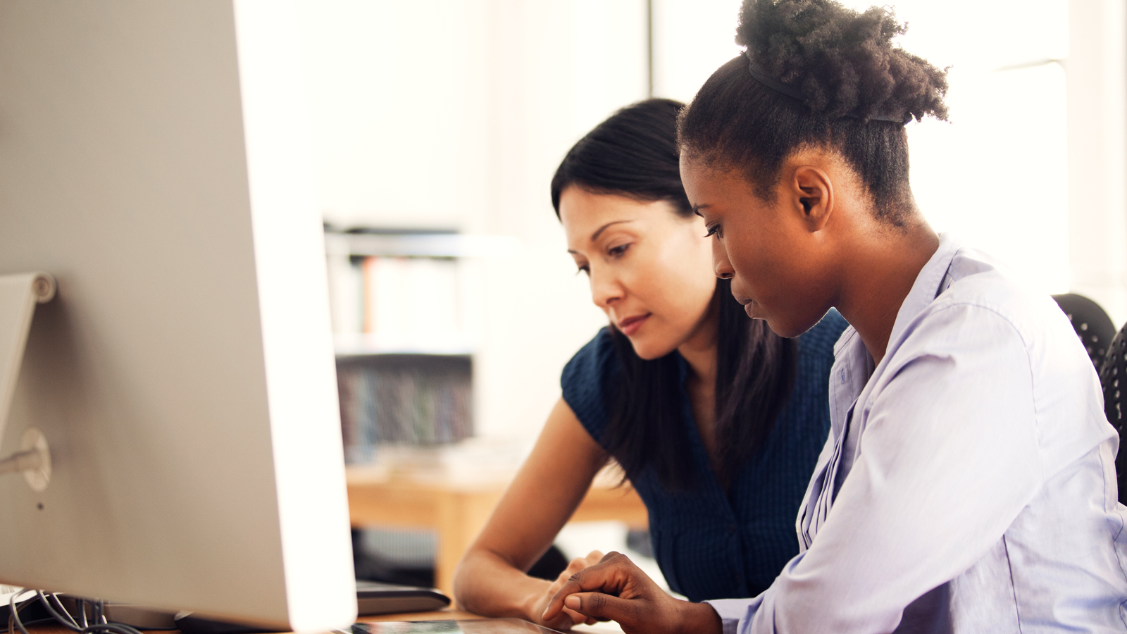 Two women sit in front of a computer and discuss content on screen. Two women sit in front of a computer and discuss content on screen.