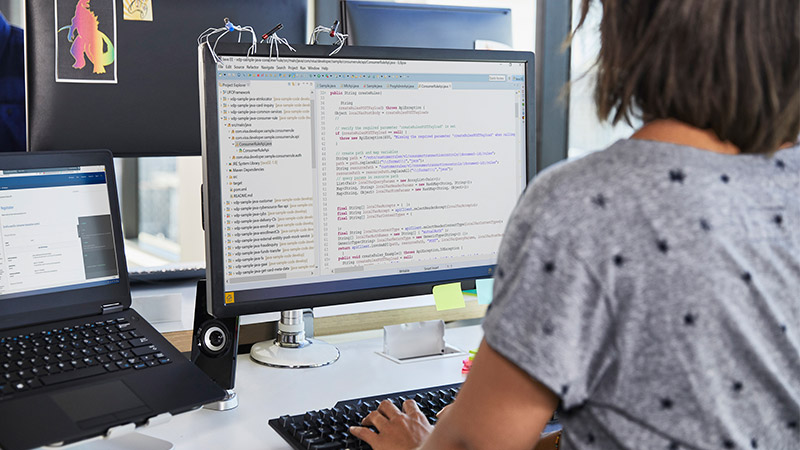 A woman sitting at her desk in front of a monitor coding.