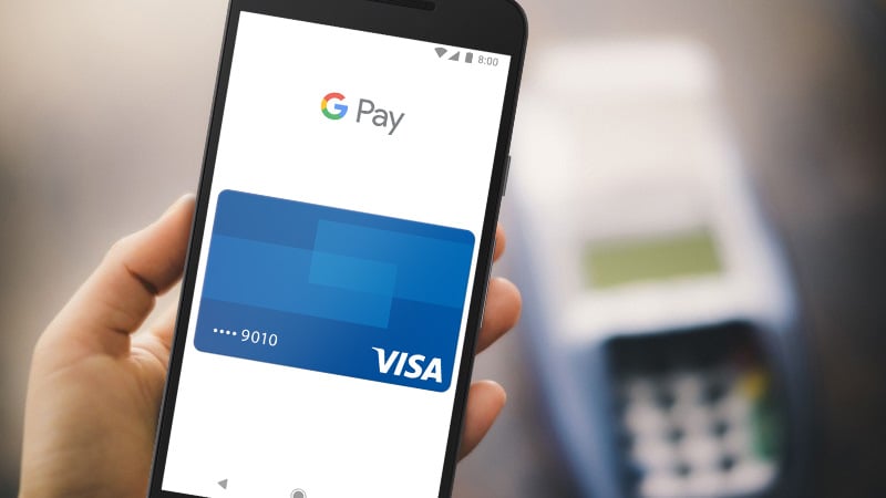 Hand holding a mobile phone with Google Pay Visa card shown on the screen.