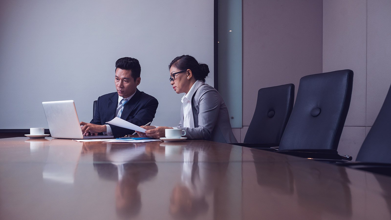 Two professionals discussing spend management while seated at a conference table with a laptop. 