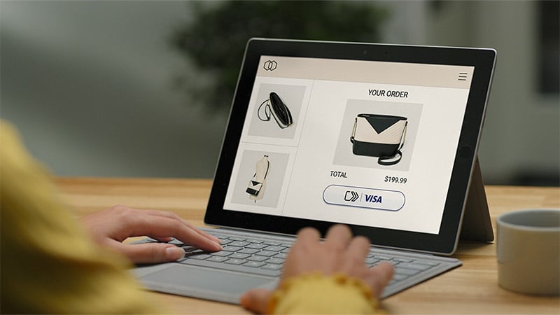 A woman is seen using her laptop to shop online. The "click to pay" button is visible on the screen, making the checkout process easy and convenient.