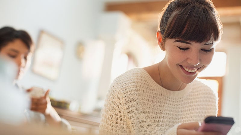 The picture of a woman grinning at her phone, satisfied with the easy and smart online checkout experience.